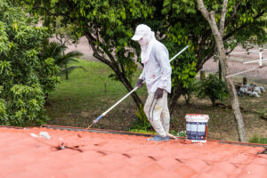 Worker painting red rooftop with roller at residential building during renovation Rensfliser